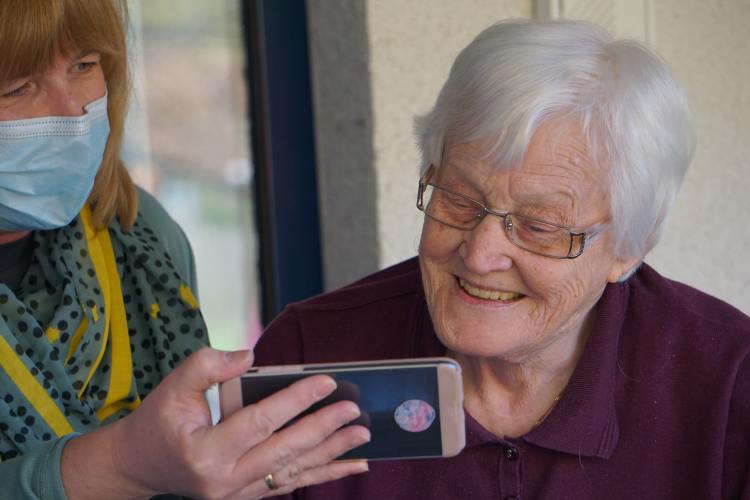 A senior woman looking at a phone held by a woman wearing a mask